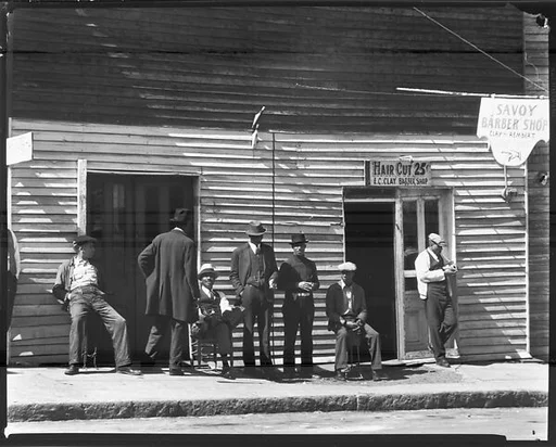 [Group of Men Seated and Standing on Sidewalk In Front of New Deal and Savoy Barber Shops, Vicksburg, Mississippi]
