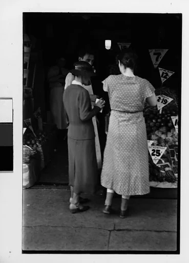 [Two 35mm Film Frames: Conversation on Street in Front of Outdoor Produce Display, Policeman Directing Traffic on Main Street]
