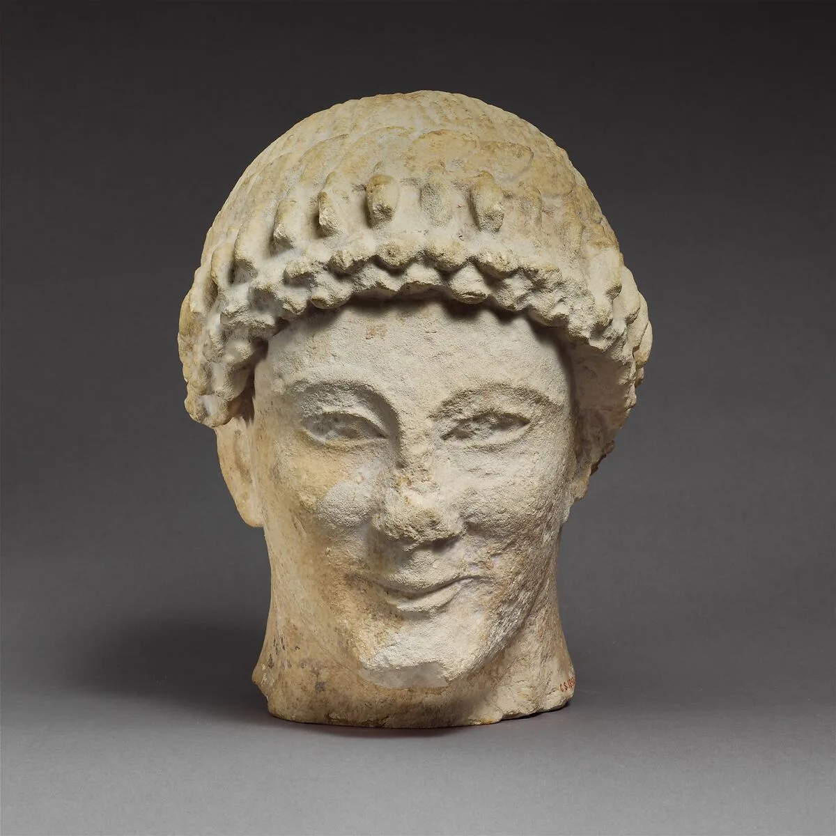 Limestone head of a beardless male with a wreath of flower buds — Unknown