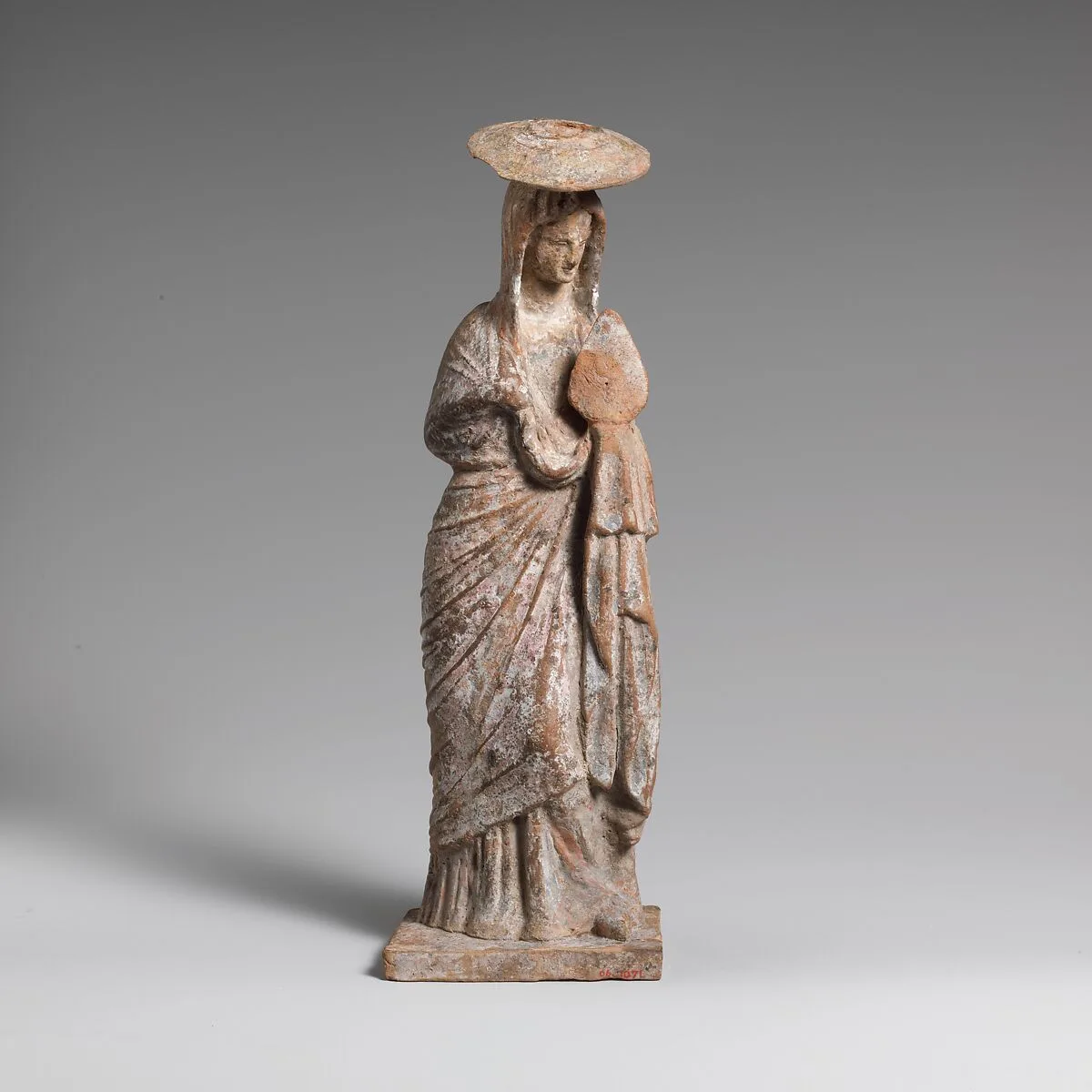 Terracotta statuette of a woman wearing a hat and holding a fan — Unknown