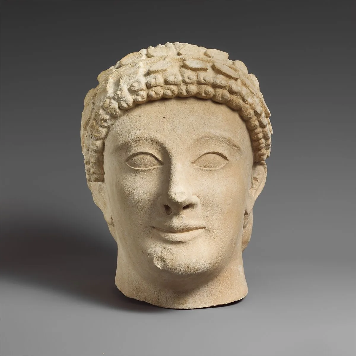 Limestone head of a beardless male votary with a wreath of leaves — Unknown