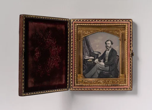 [Man Seated in Front of Cloud Backdrop, Books and Top Hat on Table]