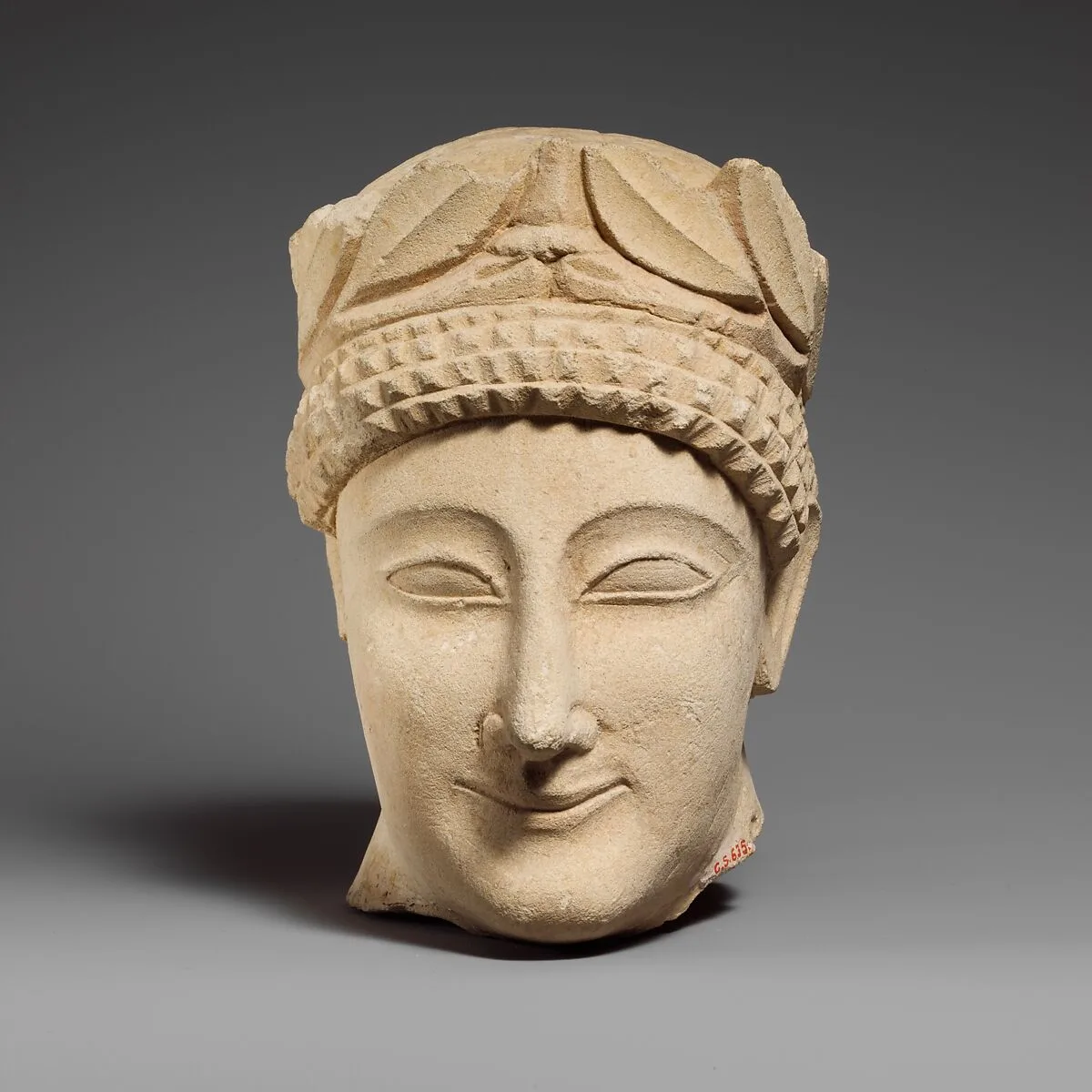 Limestone head of a beardless male votary with a wreath of leaves — Unknown