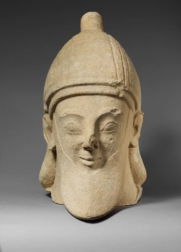 Limestone head of a bearded male wearing a conical helmet
