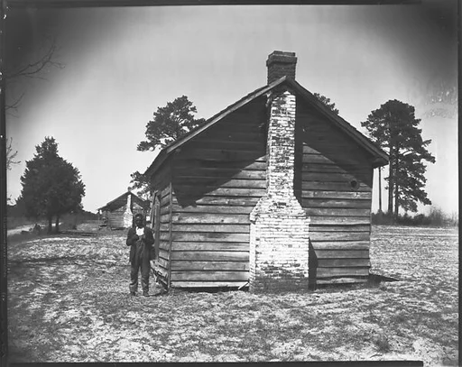 [Man Posing for Picture in Front of Wooden House]