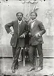 Two dapper young men leaning on a chair — Alex Agbaglo Acolatse