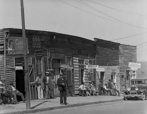 [Men Seated and Standing on Sidewalk in Front of Row of Barber Shops, Vicksburg, Mississippi]