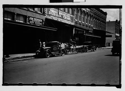 [Parked Cars and Flatbed Wagons in Front of Warehouse Buildings, Natchez, Mississippi]