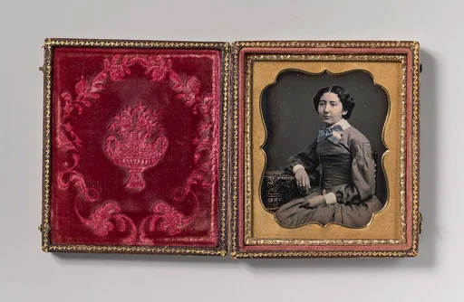 [Seated Young Woman Wearing Collar with Large Bow, Resting Arm on Table]