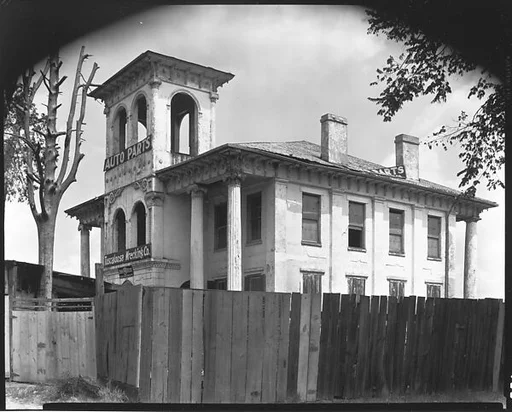 [Converted Italianate Revival House with Wrecking Company Signs on Tower Behind Wooden Fence, Near Tuscaloosa, Alabama]