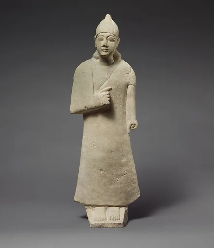Statuette of a beardless male votary wearing a long garment and a conical helmet