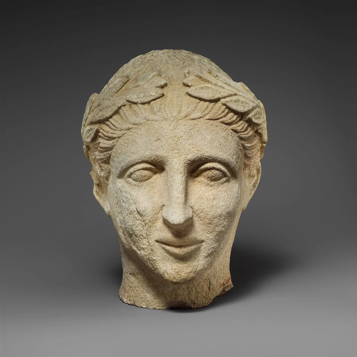 Limestone head of a beardless male votary with a wreath of leaves — Unknown