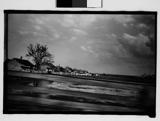 [Row of Wooden Houses Behind Slat Fence, From Moving Automobile, New Orleans Vicinity, Louisiana]