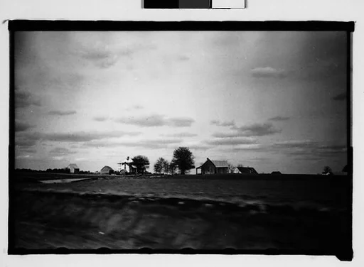 [Plantation and Surrounding Wooden Houses in Field, From Moving Automobile, Macon, Georgia]