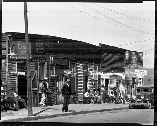 [Men Seated and Standing on Sidewalk in Front of Row of Barber Shops, Vicksburg, Mississippi]