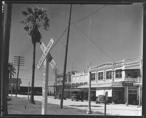 [Main Street Shopfronts and Parked Cars with Railroad Crossing Sign in Foreground, Morgan City, Louisiana]