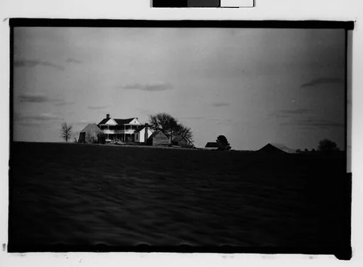 [Plantation and Surrounding Wooden Houses in Field, From Moving Automobile, Macon, Georgia]