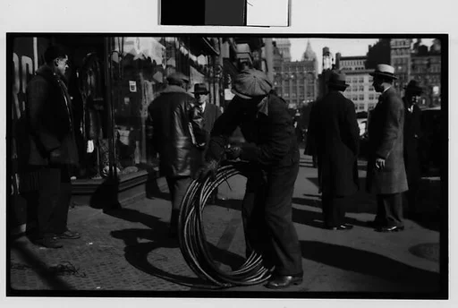 [Man Rolling Coiled Wire on Sidewalk, New York City]