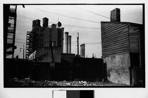 [Factory, Smokestacks, and Water Towers Behind Lot]