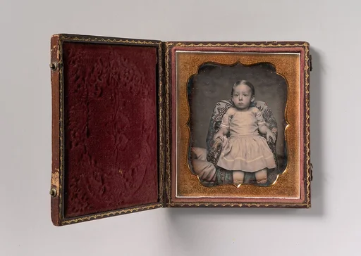 [Child Sitting on Chair Draped with Floral Print Fabric]