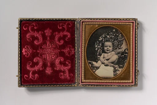 [Smiling, Nude Baby Holding Foot, Seated on Furniture Draped with Floral Print Fabric]