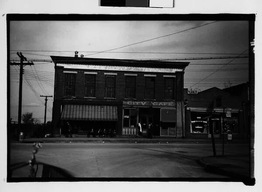 [Cafe and Drugstore on Corner with Men Seated on Bench, From Automobile, Macon, Georgia]