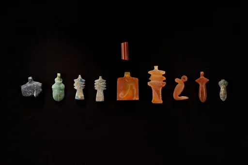 10 Amulets: 1 wedjat, 1 scarab, 3 djed pillars, 1 incised plaque, 1 uraeus, 2 wadj signs, and 1 cylindrical bead