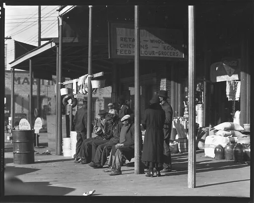 [Sidewalk Scene of Pedestrians on Bench before The Trading Post, Retail and Wholesale Store, Selma, Alabama]