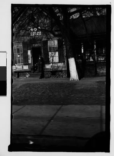 [Clapboard House with Advertisements on Façade and Two Men in Doorway, From Automobile, Macon, Georgia]