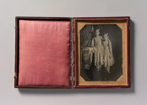 [Two Identically Dressed Young Girls Standing Next to a Table]