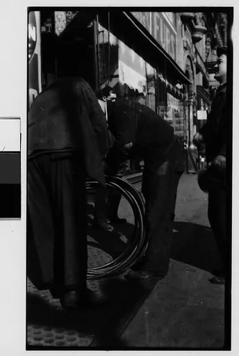 [Man Rolling Coiled Wire on Sidewalk, New York City]