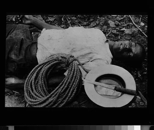 [Copy of Newspaper File Photograph: Corpse on Ground with Knife, Rope, and Straw Hat, Probably Cuba]
