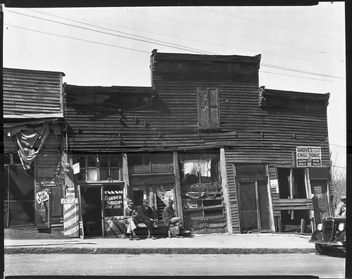 [Row of Shopfronts with Men Seated on Bench on Sidewalk, Vicksburg, Mississippi]