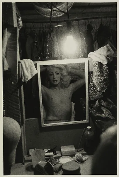Blonde female impersonator framed in a mirror beneath a light bulb, N.Y.C. — Diane Arbus