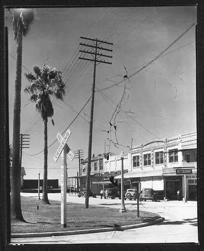 [Parked Cars and Shopfronts on Main Street with Railroad Crossing Sign and Telephone Pole in Foreground, Morgan City, Louisiana]