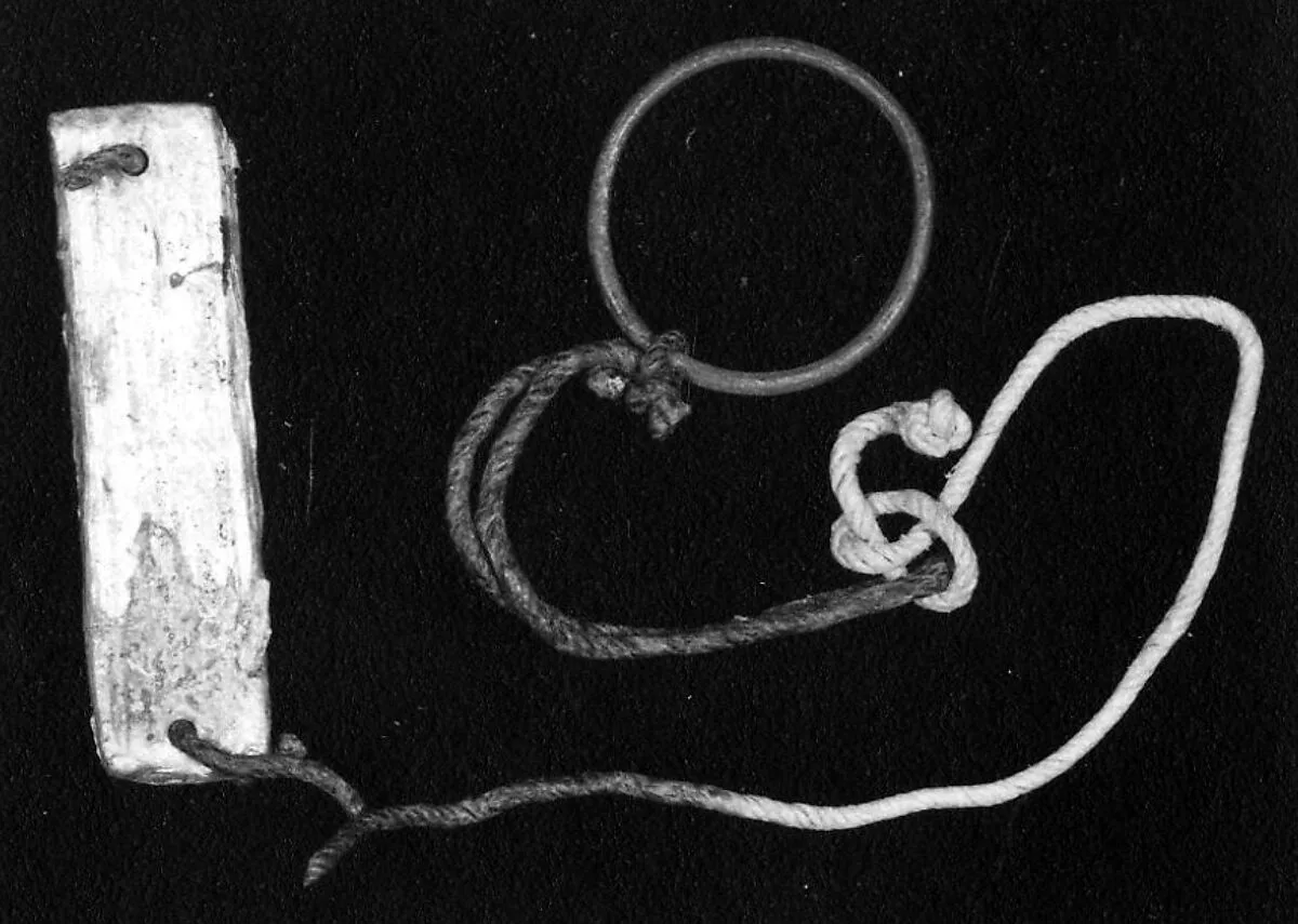A plaque tied to a bracelet or ring with a cord — Unknown