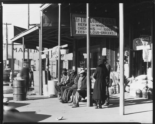 [Sidewalk Scene of Pedestrians on Bench before The Trading Post, Retail and Wholesale Store, Selma, Alabama]