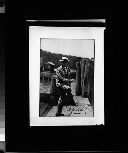 [Copy of Signed Photograph of Alfred E. Smith, Governor of New York, Standing on Dock in Suit and Hat, Eating Sandwich]
