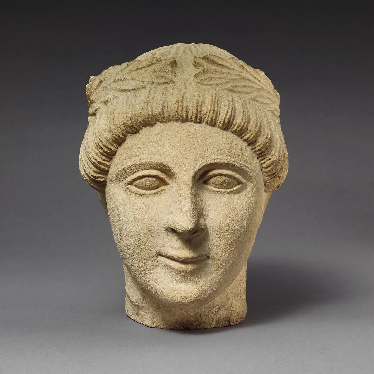 Limestone head of a beardless male votary with a wreath of leaves — Unknown