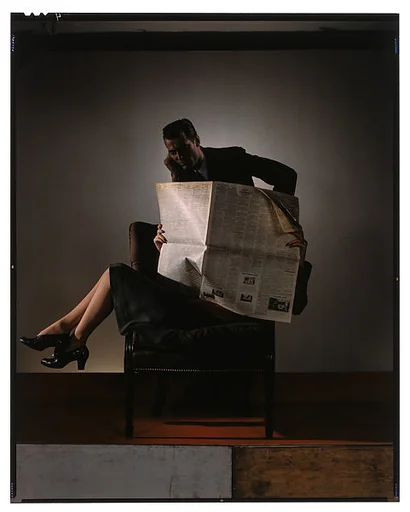 [Woman Reading Newspaper with Man Watching from Behind Chair]