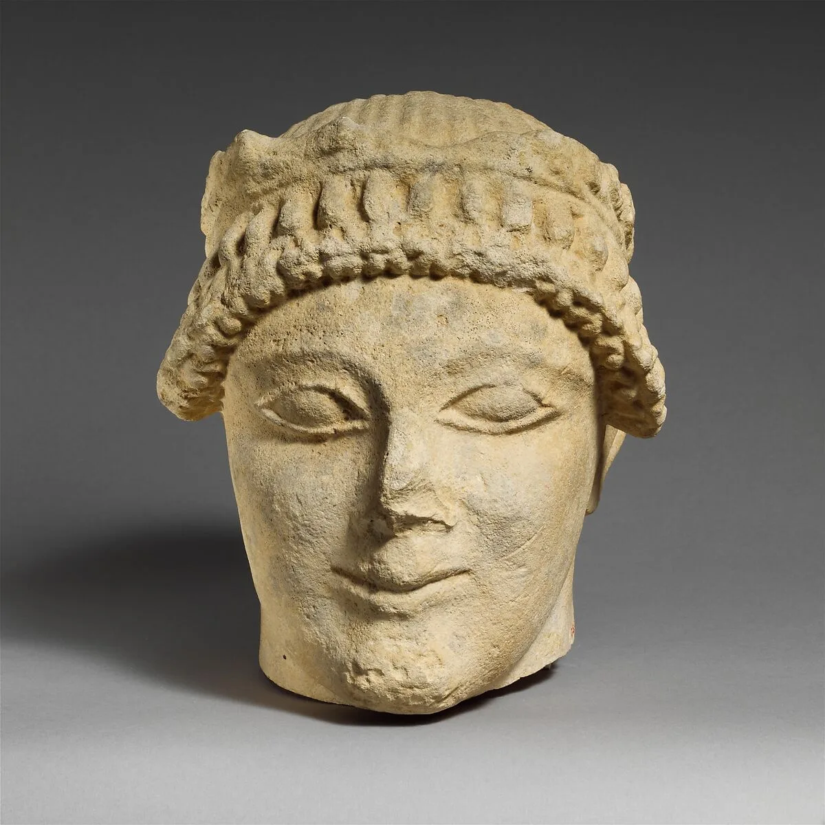 Limestone head of a beardless male votary with a wreath of leaves — Unknown