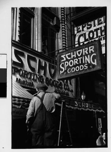 [Two 35mm Film Frames: Workman on Ladder Outside Schorr Sporting Good Company and Partial View of Man Standing in Doorway on Street, New York City]