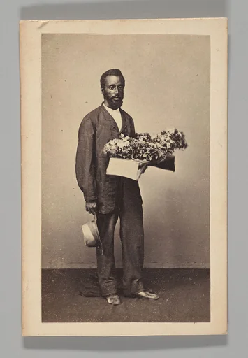 [Studio Portrait: Male Street Vendor Holding Box of Flowers, Brazil]