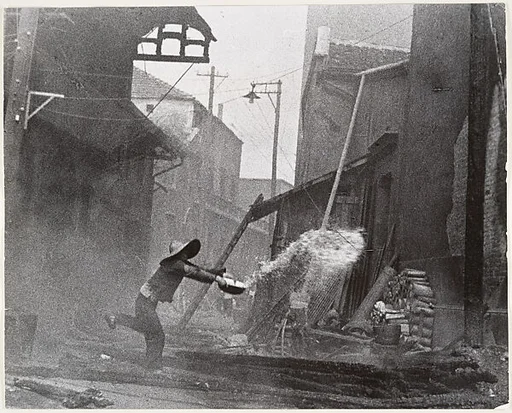 After incendiary bombardments, a woman tries futilely to extinguish the fire. Hankow