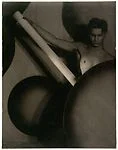 [Upper Torso of Young Male Nude, Holding Long White Rod and Posed behind Large, Dark, Circular Forms]